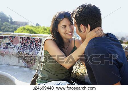 Stock Image - Young couple sitting on stone bench, portrait. Fotosearch
