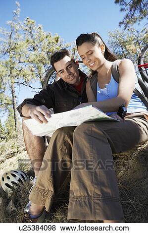 Young couple sitting outdoors reading map, low angle view. View Large Photo Image Stock Photo - Young couple sitting outdoors reading map, low angle view.. Fotosearch