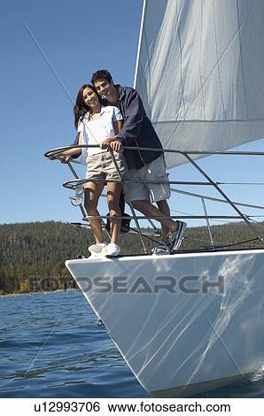 Stock Photograph - Young couple standing on bow of sailboat. Fotosearch