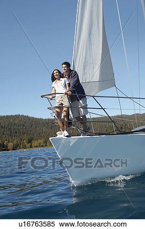 Stock Photography - Young couple standing on bow of sailboat. Fotosearch