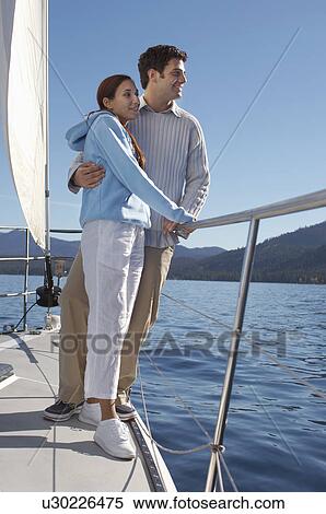 Stock Photography - Young couple standing on bow of sailboat. Fotosearch