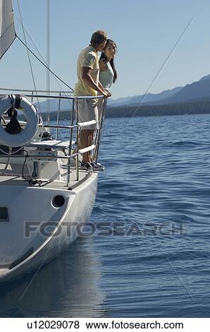 Stock Photo - Young couple standing on side of sailboat. Fotosearch