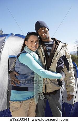 Stock Image - Young couple standing outdoors with tents in background.. Fotosearch