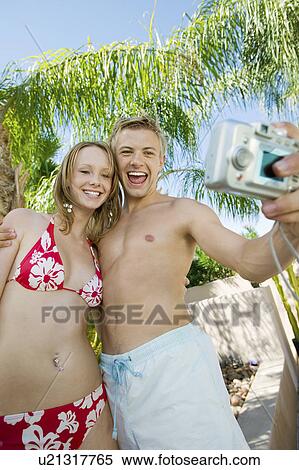 Stock Photography - Young couple taking photo of themselves, low angle view. Fotosearch