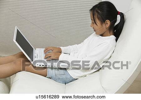 Stock Photo - Young Girl in Chair Using Laptop, side view. Fotosearch
