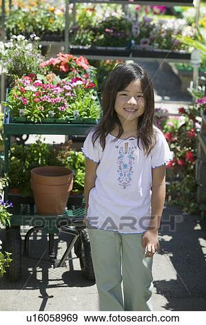 Young girl standing in plant nursery, portrait View Large Photo Image Stock Photo - Young girl standing in plant nursery, portrait. Fotosearch