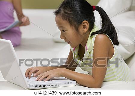 Stock Photo - Young Girl Using Laptop on sofa, close up, side view. Fotosearch