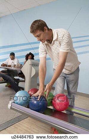 Stock Image - Young man at bowling alley choosing ball. Fotosearch