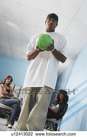Stock Image - Young man at bowling alley holding ball, portrait, low angle view. Fotosearch