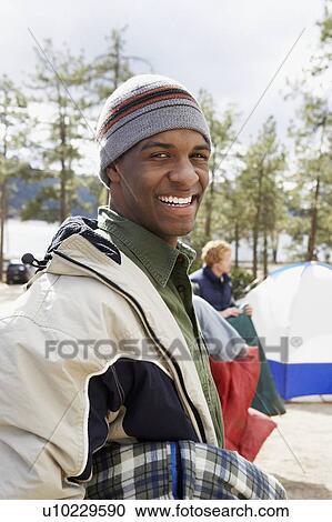 Stock Image - Young man at campsite, portrait, half length. Fotosearch