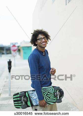 Stock Photography - Young man carrying skateboard in street, portrait. Fotosearch