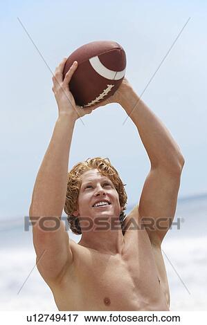 Stock Photo - Young man catching football on beach. Fotosearch