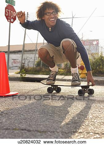 Young man crouching on skateboard in street View Large Photo Image Stock Image - Young man crouching on skateboard in street. Fotosearch