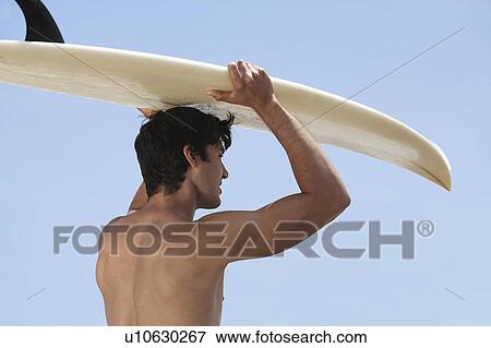 Stock Photo - Young man holding surfboard over head, back view. Fotosearch