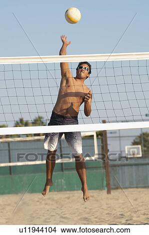 Young man jumping, hitting volleyball over net on beach View Large Photo Image Picture - Young man jumping, hitting volleyball over net on beach. Fotosearch