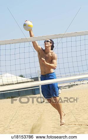 Young man jumping, hitting volleyball over net on beach View Large Photo Image Stock Photograph - Young man jumping, hitting volleyball over net on beach. Fotosearch