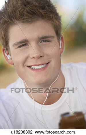 Stock Image - Young man listening to mp3 player, portrait, (portrait). Fotosearch