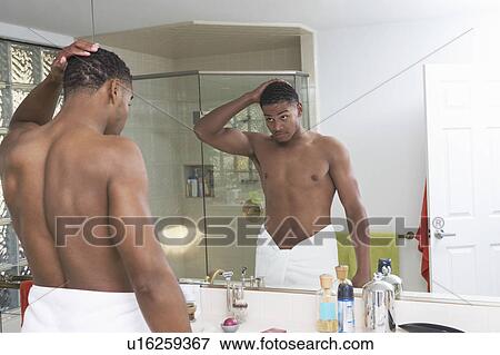 Stock Photo - Young man looking at self in bathroom mirror. Fotosearch