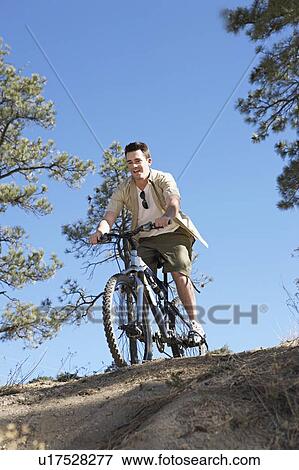 Young man mountain biking over top of hill, low angle view. View Large Photo Image Stock Photo - Young man mountain biking over top of hill, low angle view.. Fotosearch