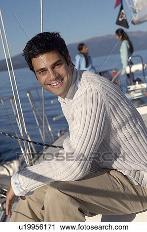 Young man on sailboat, friends in background, (portrait) View Large Photo Image Stock Image - Young man on sailboat, friends in background, (portrait). Fotosearch