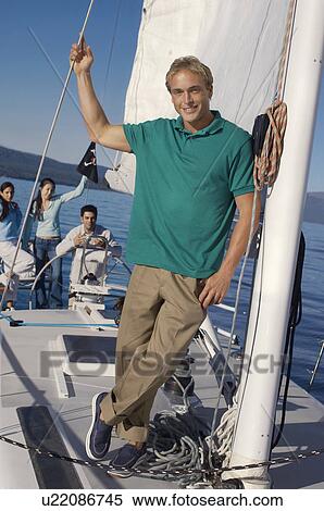 Stock Photography - Young man on sailboat, friends in background, (portrait). Fotosearch
