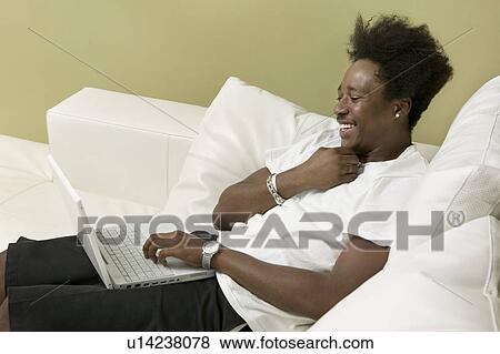 Young man on sofa using laptop, side view View Large Photo Image Stock Photo - Young man on sofa using laptop, side view. Fotosearch