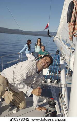 Young man raising sail on sailboat, friends in background View Large Photo Image Stock Image - Young man raising sail on sailboat, friends in background. Fotosearch