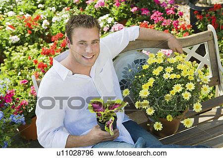 Stock Photograph - Young man resting on bench in garden centre, (portrait), (elevated view). Fotosearch