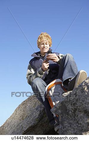 Young man sitting on boulder, using compass, low angle view. View Large Photo Image Stock Photo - Young man sitting on boulder, using compass, low angle view.. Fotosearch