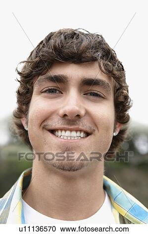 Stock Image - Young man smiling outside, close-up, portrait. Fotosearch