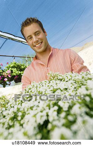 Stock Photo - Young man standing in greenhouse, (portrait), (low angle view). Fotosearch