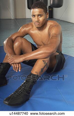 Stock Image - Young muscular man sitting on training mat in gym. Fotosearch