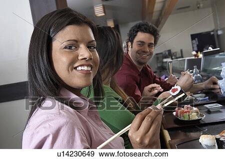 Stock Photo - Young people eating sushi with chopsticks in restaurant. Fotosearch