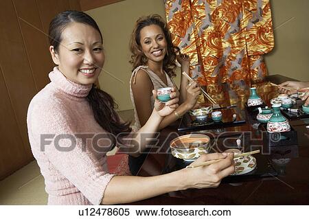 Stock Photography - Young people holding saki cups in Japanese restaurant. Fotosearch