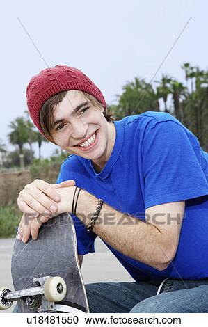 Stock Image - Young skateboarder sitting outside, portrait. Fotosearch