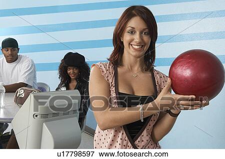 Stock Photo - Young woman at bowling alley holding ball, portrait. Fotosearch