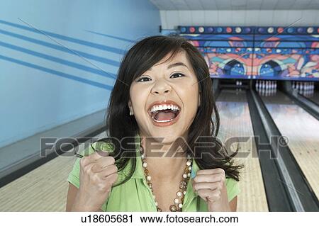 Stock Image - Young woman at bowling alley celebrating, portrait. Fotosearch