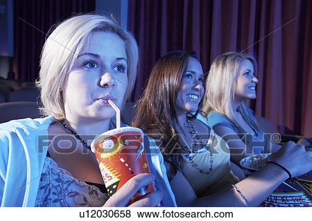 Stock Photo - Young woman drinking soft drink, sitting with Friends, Watching Movie in theatre. Fotosearch