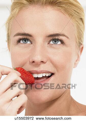 Stock Image - Young Woman Eating Strawberry, close up, head shot. Fotosearch
