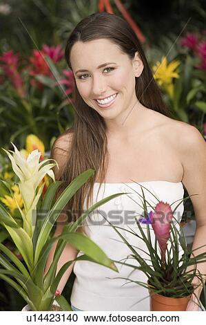 Stock Image - Young woman holding exotic potted plants, (portrait). Fotosearch