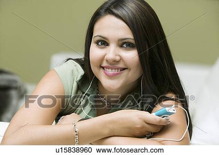 Stock Image - Young woman lying on sofa listening to MP3 player, portrait, close up. Fotosearch