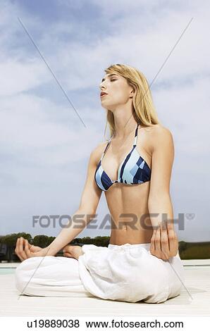 Stock Photo - Young woman meditating in lotus position on outdoor deck, ground view. Fotosearch