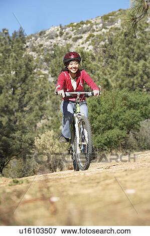 Stock Photo - Young Woman Mountain Biking in field, front view.. Fotosearch