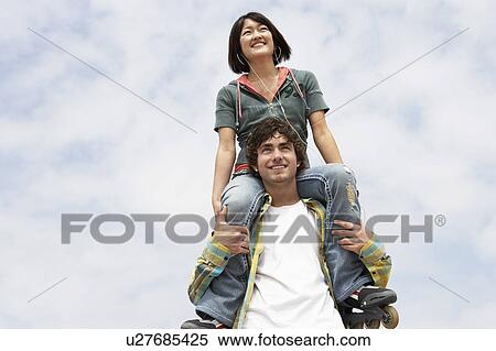 Stock Photography - Young woman on shoulders of man, low angle view. Fotosearch