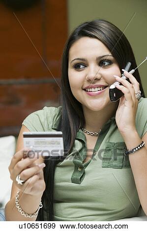 Stock Photo - Young woman on sofa making purchase with credit card on mobile phone. Fotosearch