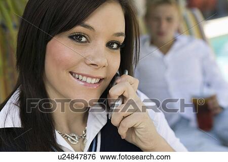 Stock Photograph - Young woman sitting by pool on cell phone, portrait, close up. Fotosearch