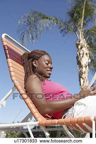 Young woman sitting in sunlounger reading, low angle view View Large Photo Image Stock Image - Young woman sitting in sunlounger reading, low angle view. Fotosearch
