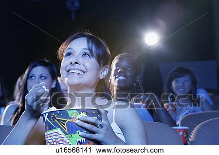 Young woman sitting in theatre, eating popcorn, watching movie View Large Photo Image Stock Image - Young woman sitting in theatre, eating popcorn, watching movie. Fotosearch