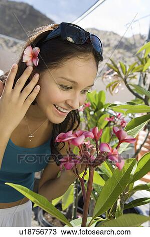 Stock Image - Young woman smelling exotic plat in greenhouse, (close-up). Fotosearch
