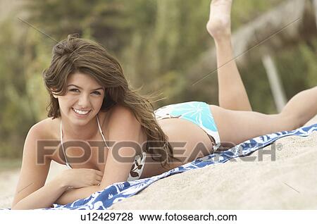 Stock Photo - Young Woman smiling, lying down on Beach, portrait, tilt view. Fotosearch